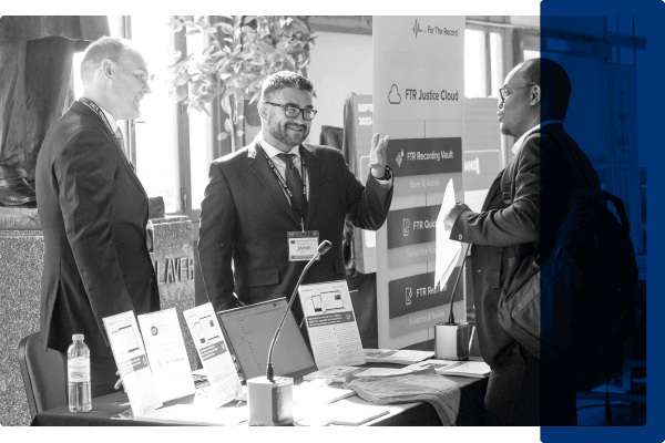 A black and white image of three men talking at a conference booth